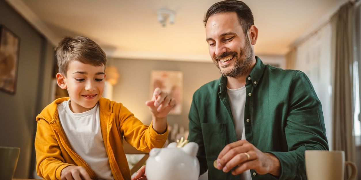 Father and son put coins together in piggy bank