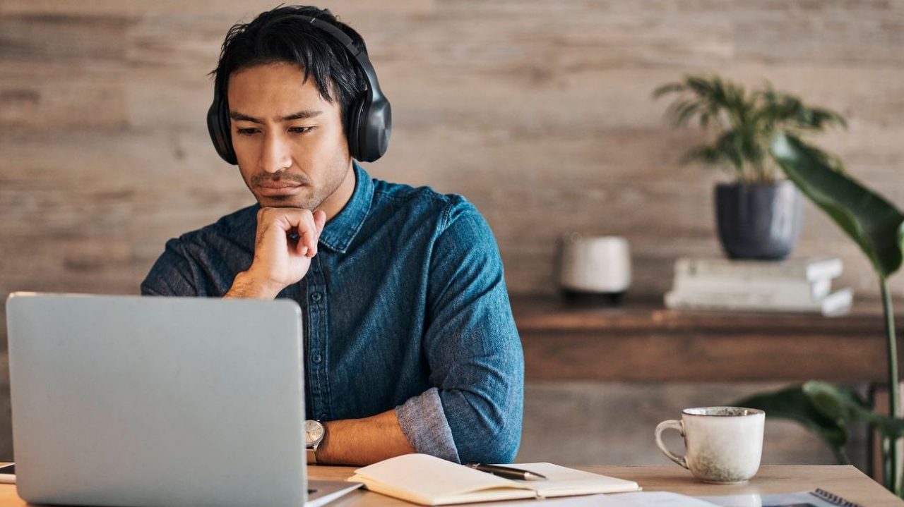 Young adult male professional wearing headphones and looking at a laptop
