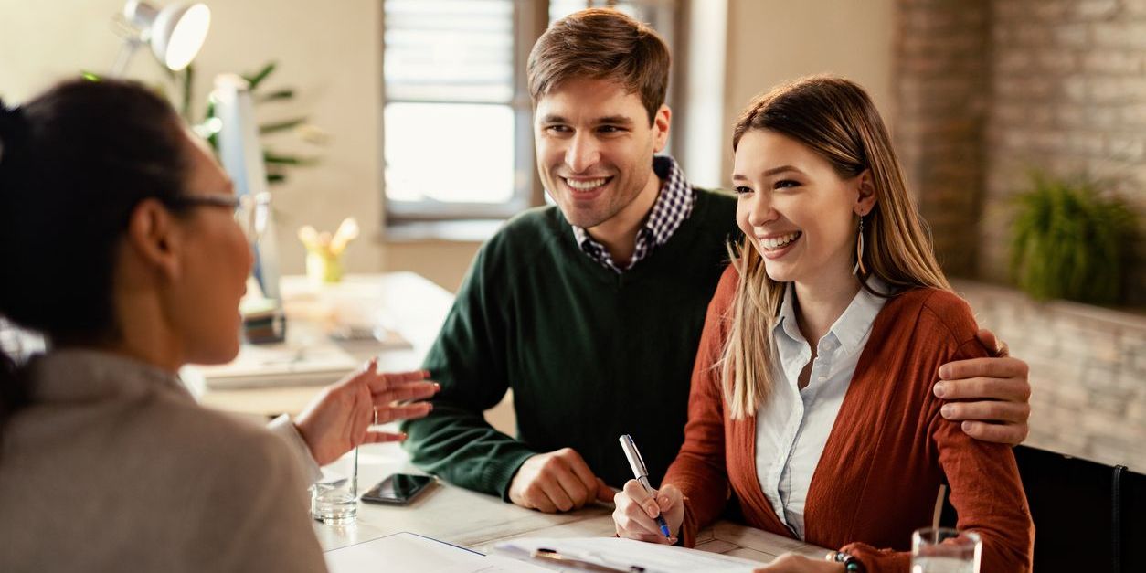 Young happy couple signing a contract while being on a meeting with insurance agent in the office.