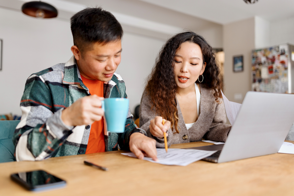 Young Asian couple in their kitchen with a laptop analyzing finances
