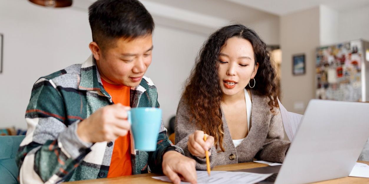 Young Asian couple in their kitchen with a laptop analyzing finances