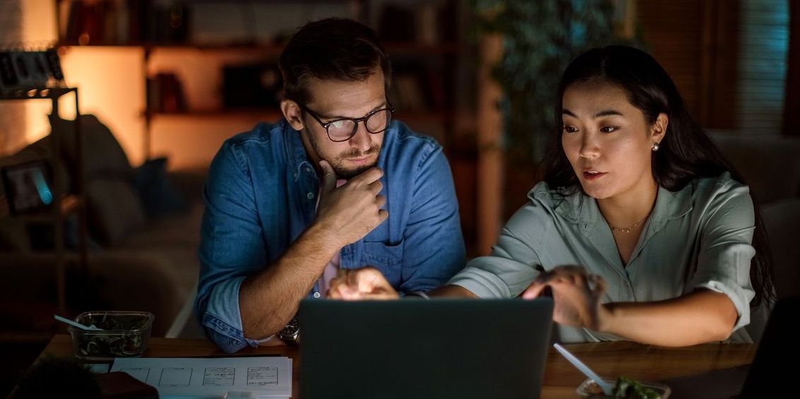 Mixed couple at home looking at their investments on a laptop at nighttime