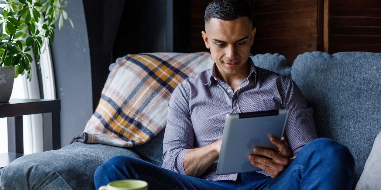 Young adult male investor on the couch studying his tablet