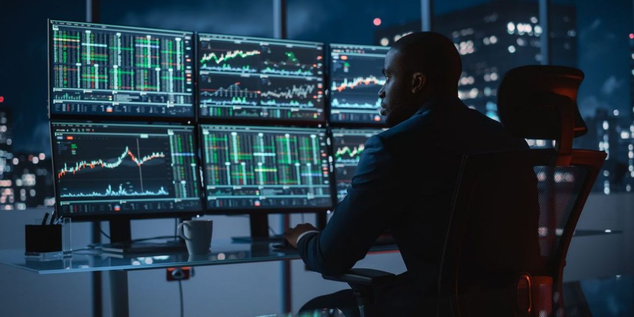African American male analyst looking at multiple market screens