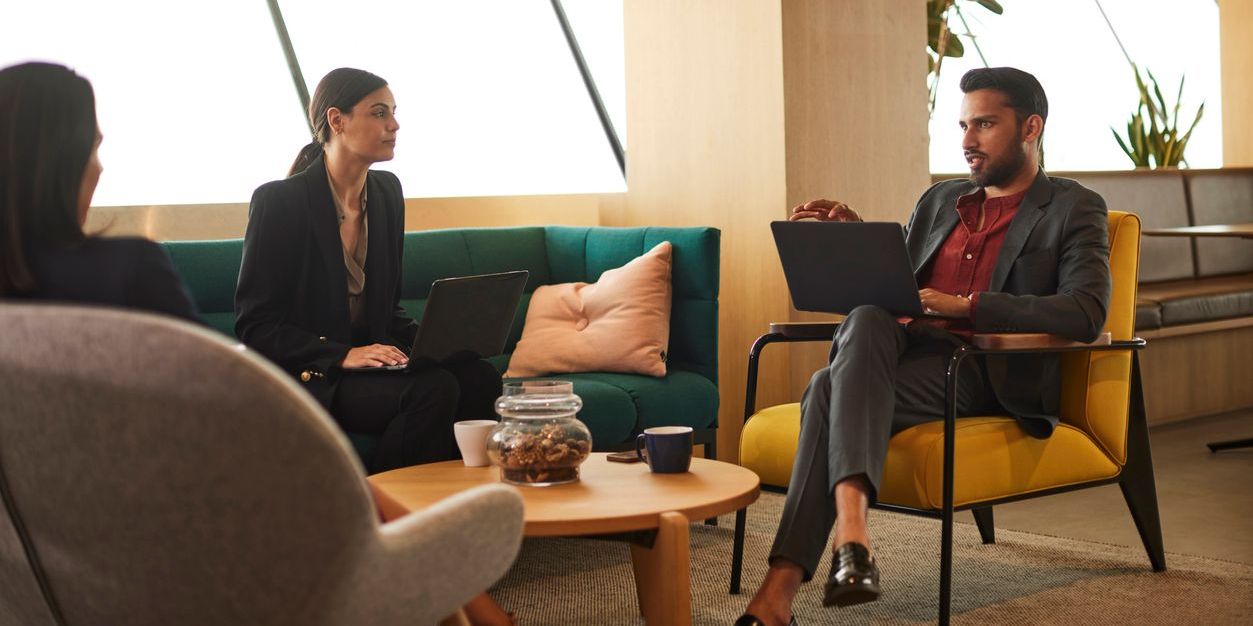 Three financial professionals with laptops meeting in a casual, colorful space