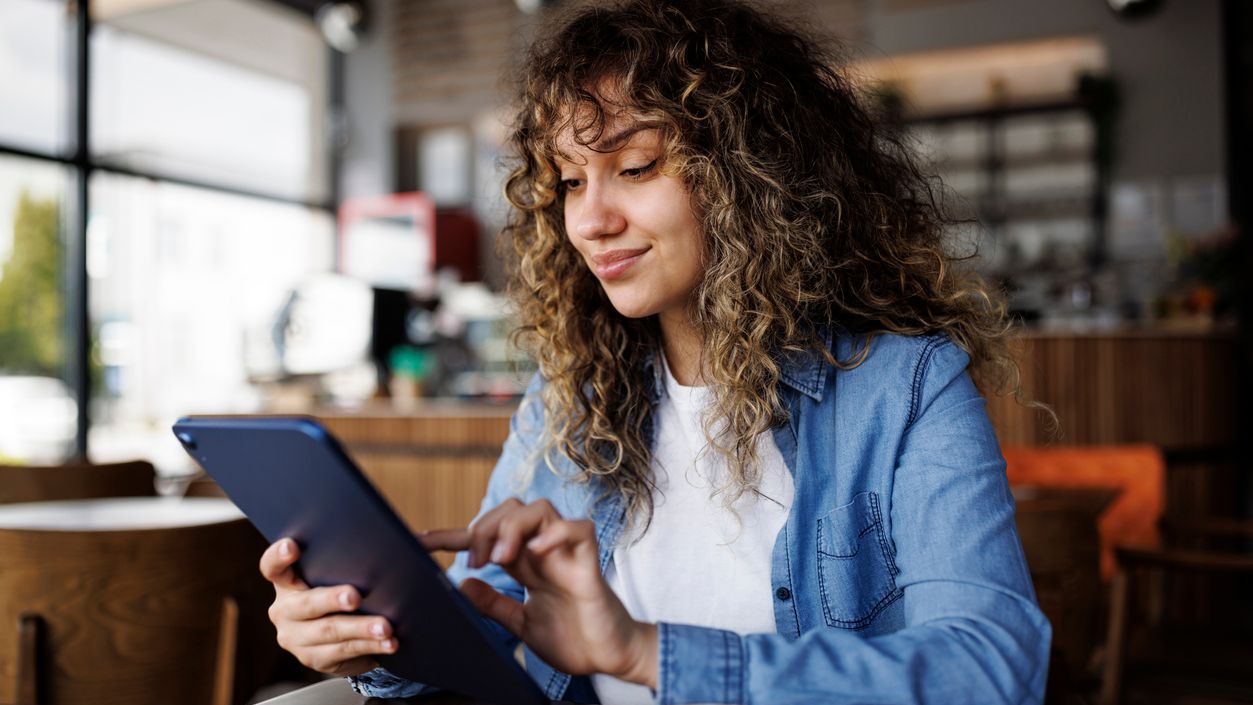 Young adult woman looking at mutual funds on a tablet in a coffee shop
