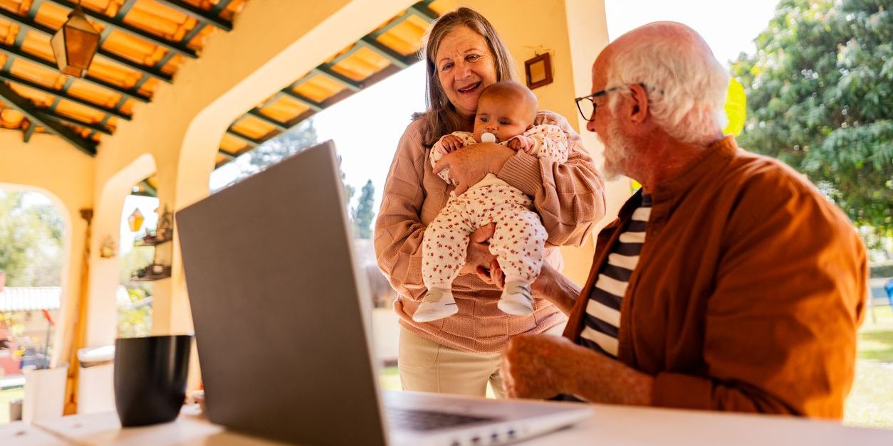 Senior man talking to his wife while she holds their baby granddaughter at home