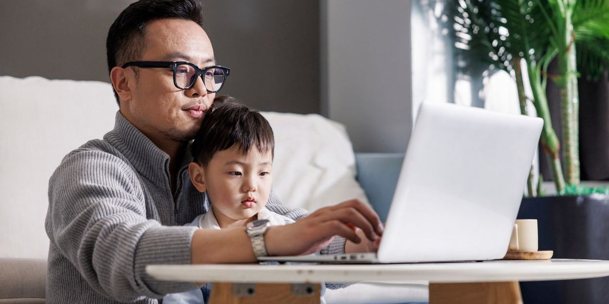 Asian father with his toddler in his lap while working on a laptop